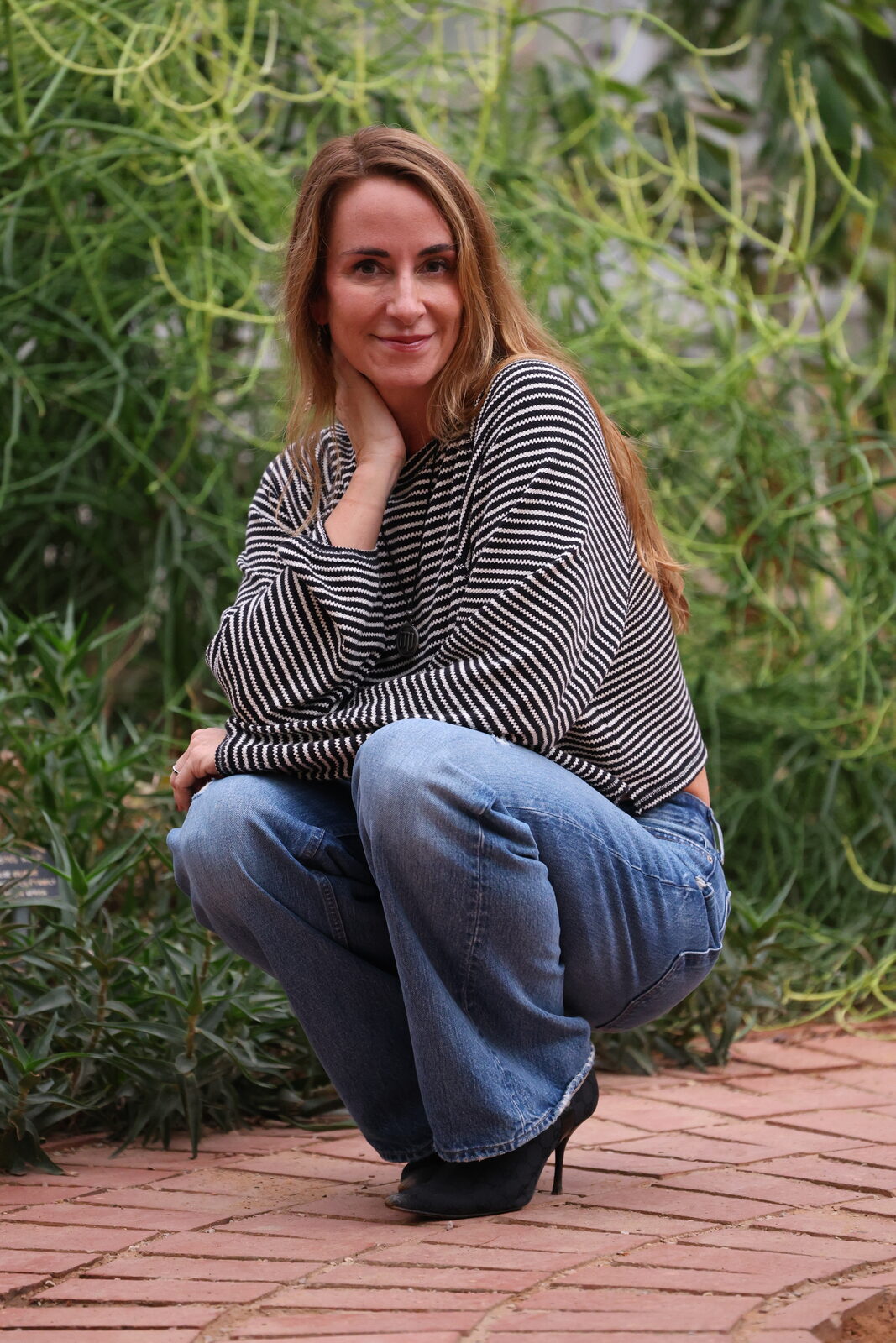 Tracey Abbott crouched among desert plants in a striped sweater
