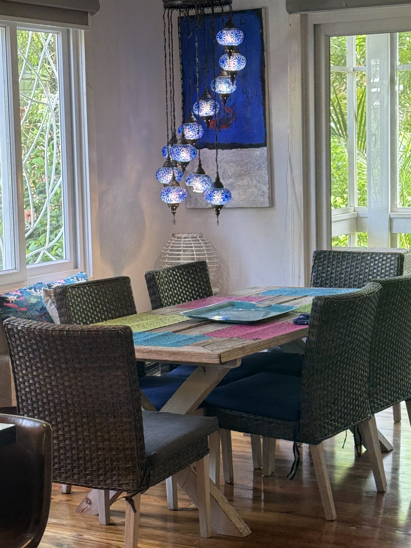 The long dining table in the house, blue mosaic lamps hanging in the corner, jungle through the windows