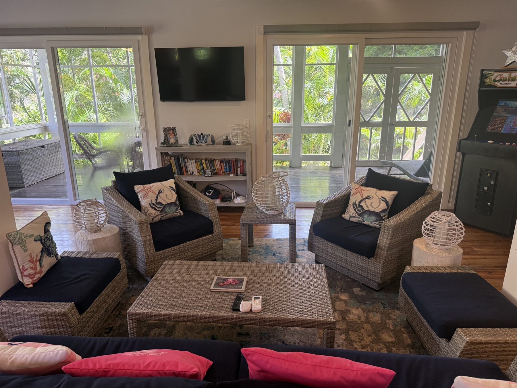 The living room, wicker chairs with navy cushions around a low table, screened porch and palms beyond