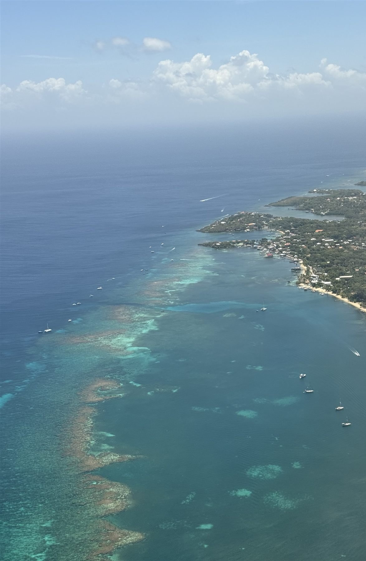 Aerial view of Roatan from the plane, the reef and turquoise shallows tracing the green island coastline